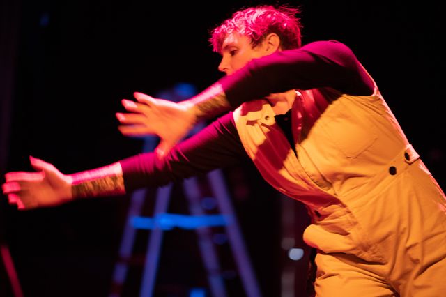 Miriam in yellow short-sleeve overalls and theater lighting
reaches dramatically out across her body.
