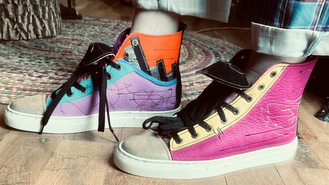 Low angle of my feet in brightly colored shoes.
Right foot inside has lavender low-top with blue lining
that transitions to silver/black stripes and orange upper.
Left foot outside is magenta with yellow lace panel.
Both have a mix of tan stitched art,
black stitched horizontal lines,
and red stitched scribbles.