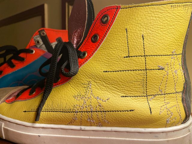 Closeup outside left shoe
in yellow leather with orange lace panel,
two tan-stitched close-wing moth sketches,
with black lines and arrows.