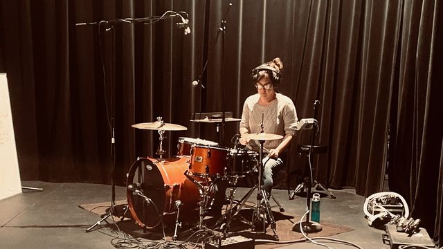 Sondra sitting behind the drum kit, surrounded by mics and cables, ready to record